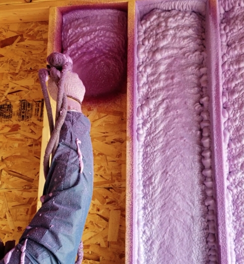 worker applying spray foam insulation on interior residential build